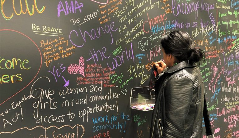 Woman writing on a blackboard covered with positive messages about changing the world.